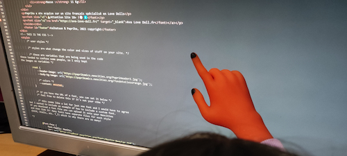 Main de poupée à la peau rouge pointant du code html sur un écran d'ordinateur.