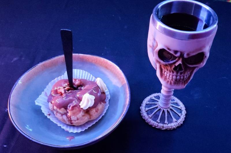 photo d'un dessert au chocolat dans une petite assiette creuse et d'un verre en forme de colonne vertebrale et de crâne avec du jus de raisin dedans.